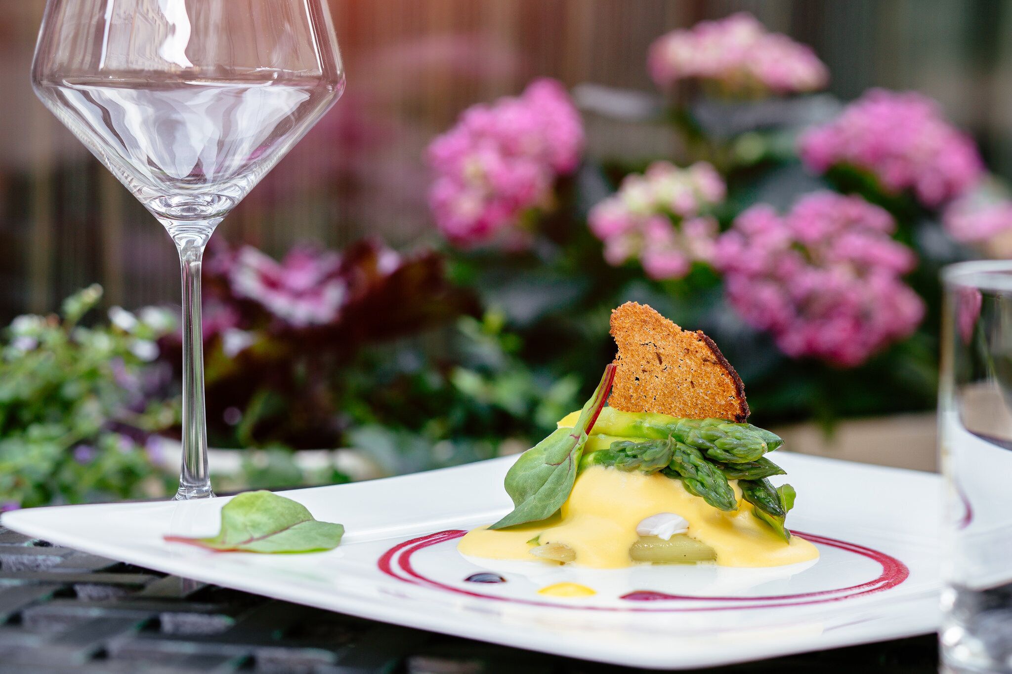 A plate of food with a glass of wine, set against a blurred background of flowers.