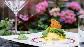 A plate of food with a glass of wine, set against a blurred background of flowers.