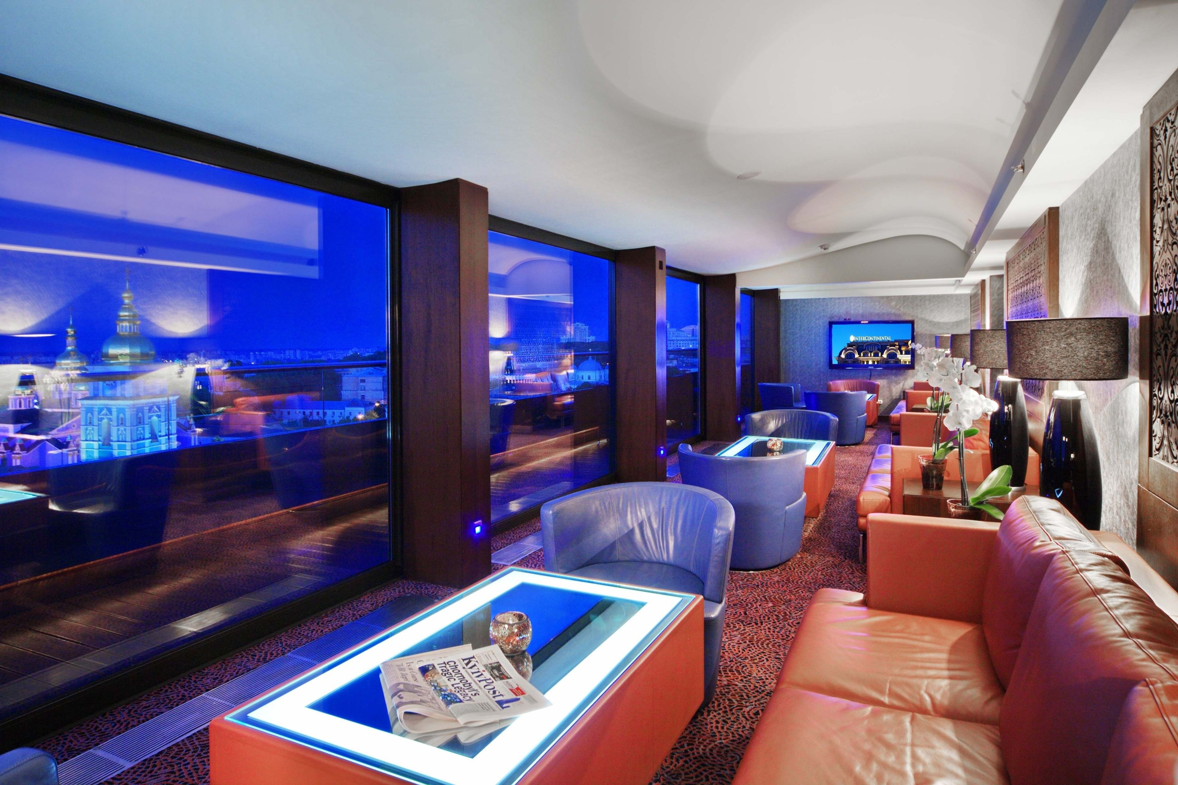 Un hall d’hôtel moderne avec vue sur la ville, des fauteuils en cuir et un téléviseur.