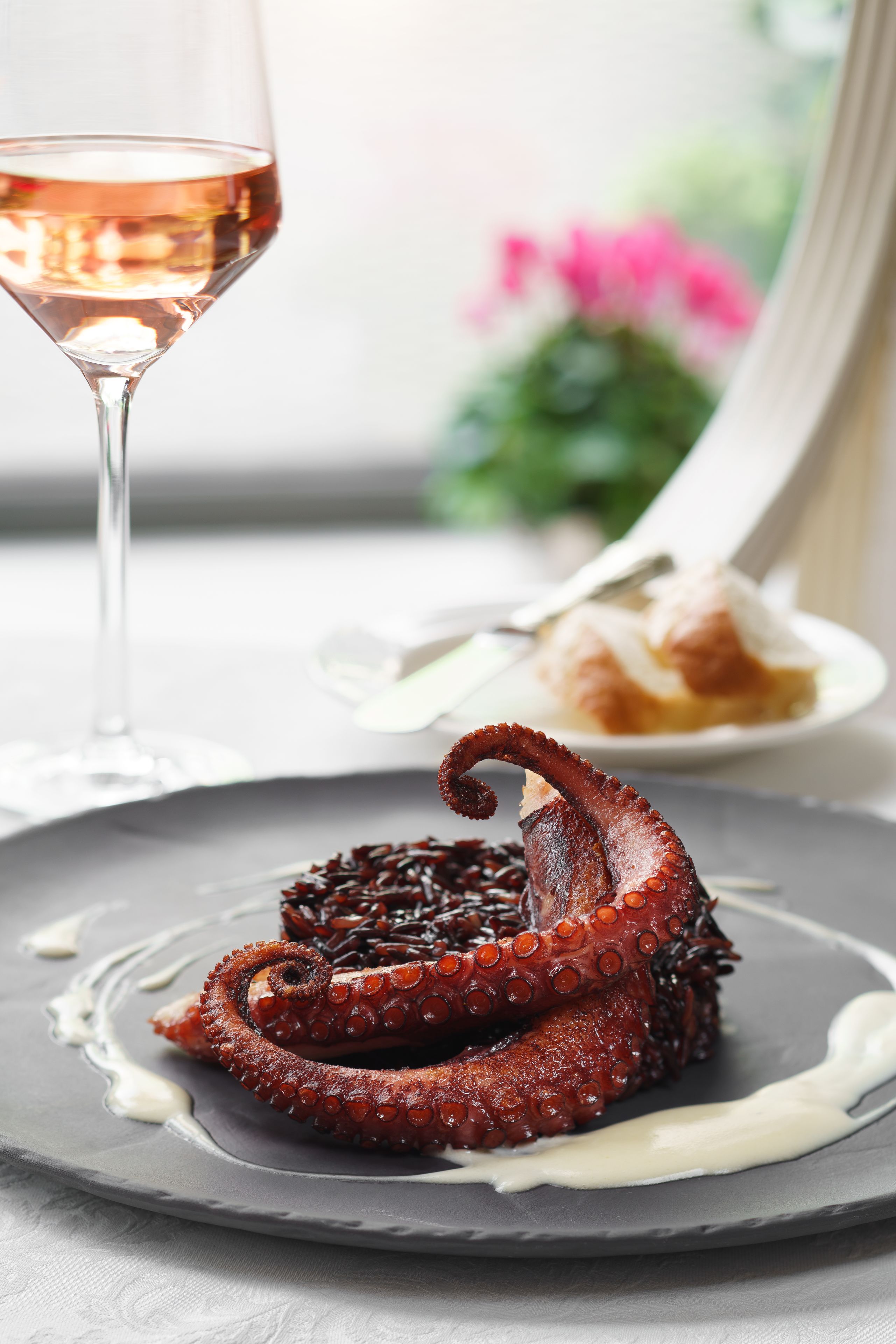 A plate of octopus with a sauce, a glass of wine, and a plate of food in the background.