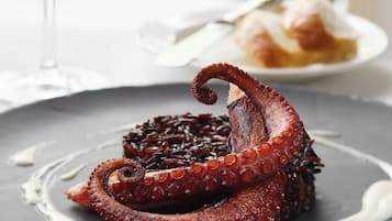 A plate of octopus with a sauce, a glass of wine, and a plate of food in the background.