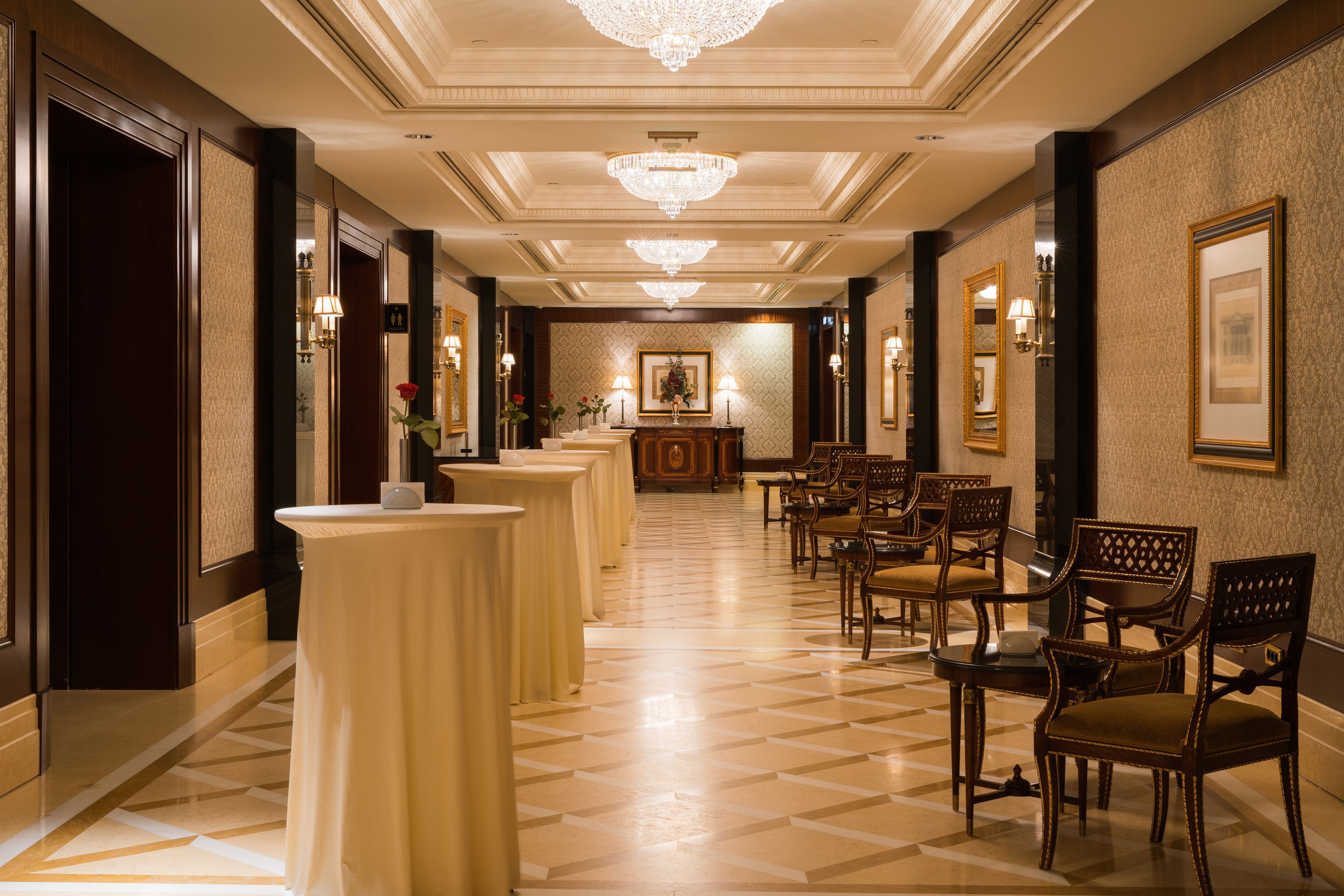 Un vestíbulo de hotel con piso a cuadros, candelabros, obras de arte enmarcadas y una mesa de recepción.