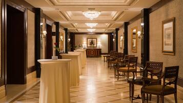 Un vestíbulo de hotel con piso a cuadros, candelabros, obras de arte enmarcadas y una mesa de recepción.