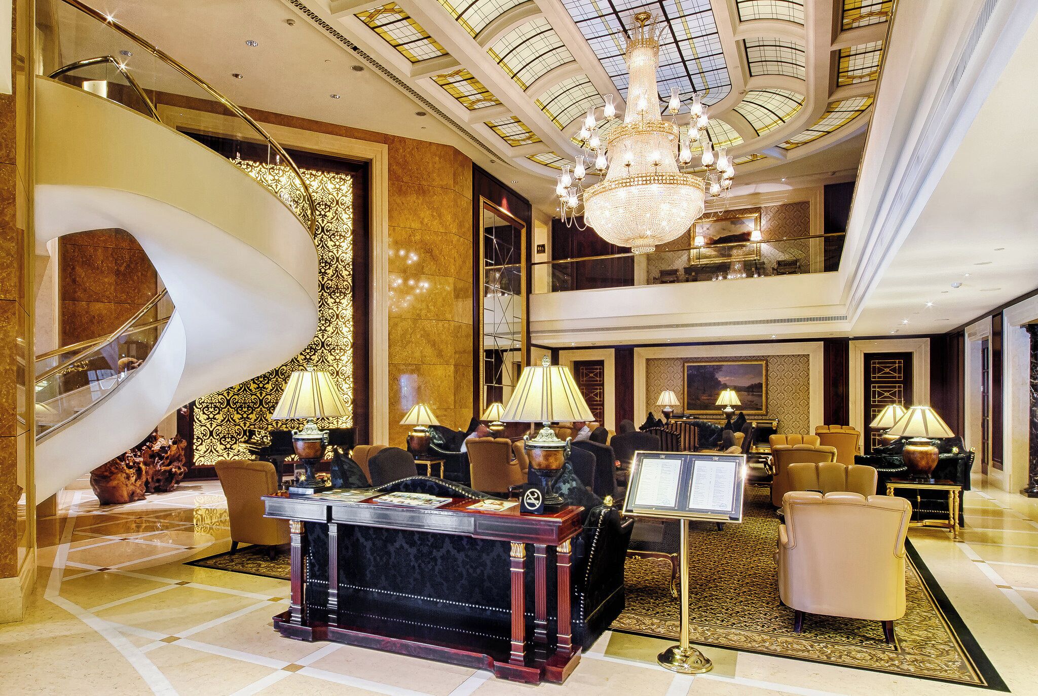 A luxurious lobby with a grand staircase, elegant furniture, and a chandelier.