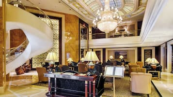 A luxurious lobby with a grand staircase, elegant furniture, and a chandelier.