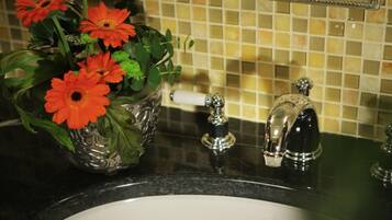 A bathroom with a sink, a decorative glass vase with flowers, a mirror, and a tiled backsplash.