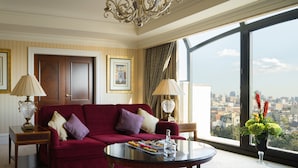 A spacious room with a red sofa, two lamps, a coffee table with snacks, and a large window offering a city view. - InterContinental Kyiv by IHG (Kyiv)