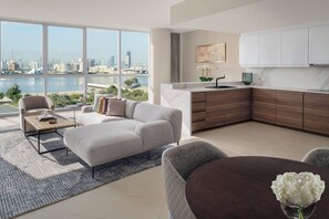 Un salon moderne doté d’une grande fenêtre, d’un canapé, d’une table basse et offrant une vue sur les toits d’une ville et sur l’eau.