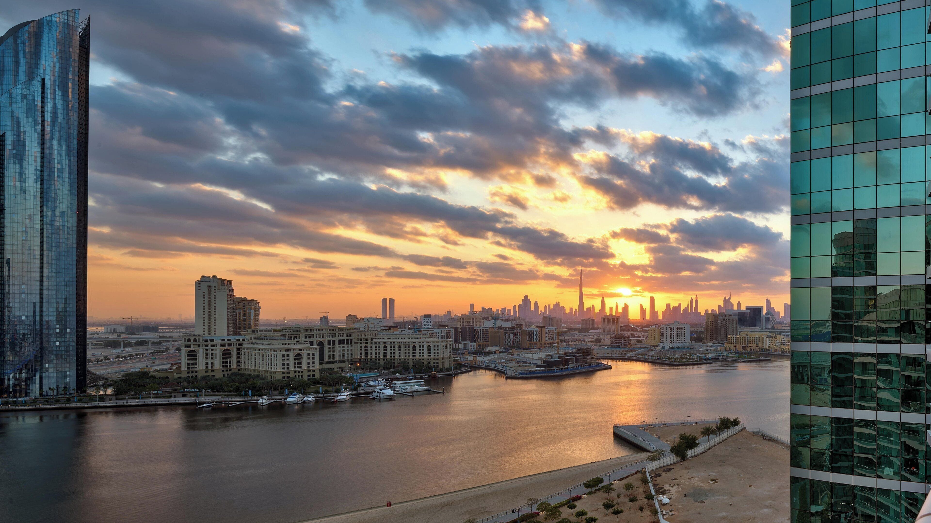 A cityscape with a river, modern buildings, and a sunset.