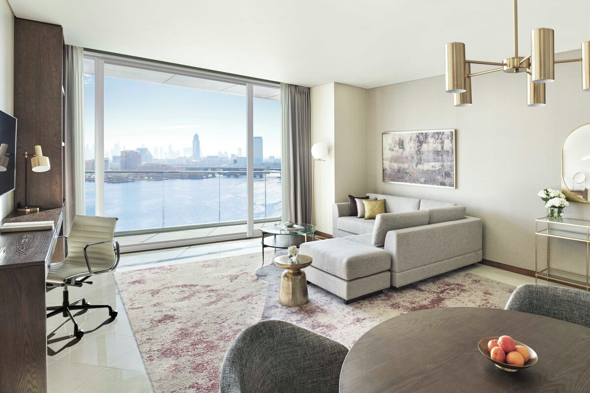 Ein modernes Wohnzimmer mit großem Fenster, einer Couch, einem Esstisch mit Obst und Blick auf die Stadt.