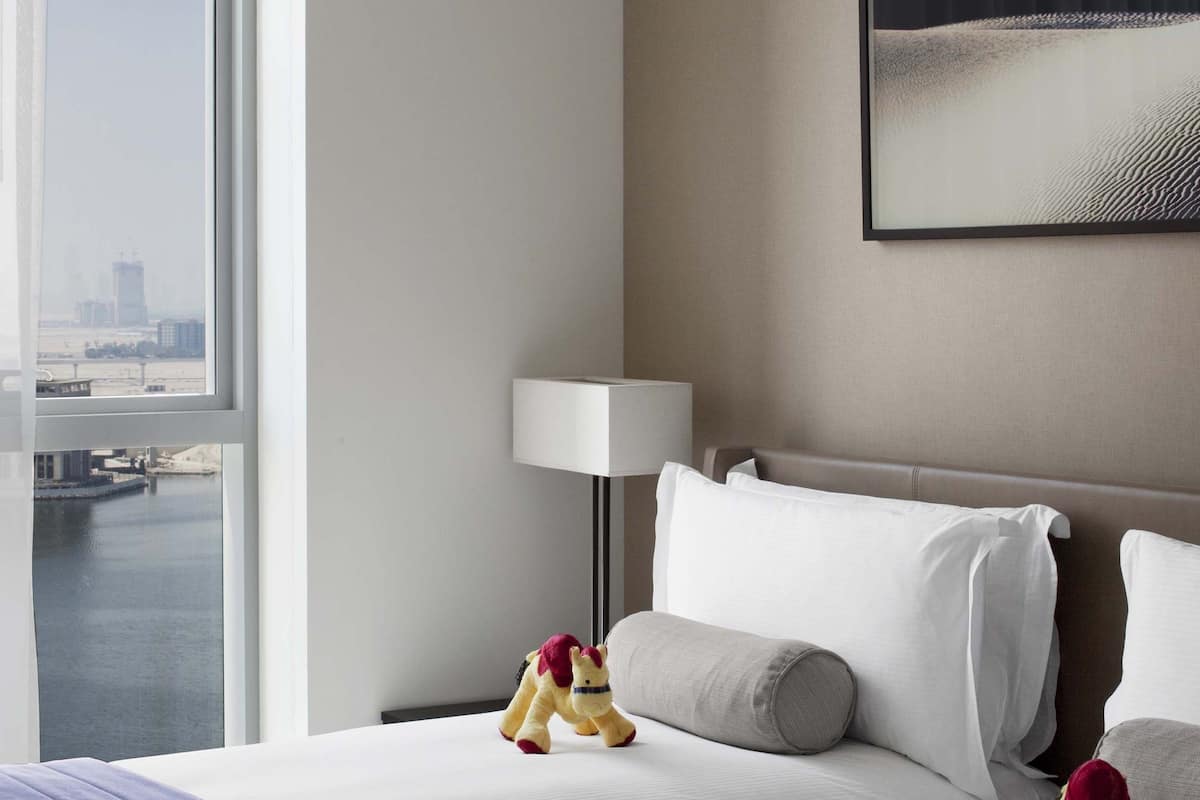 Une chambre d’hôtel avec deux lits, une vue sur la ville, une lampe et un tableau encadré au mur.