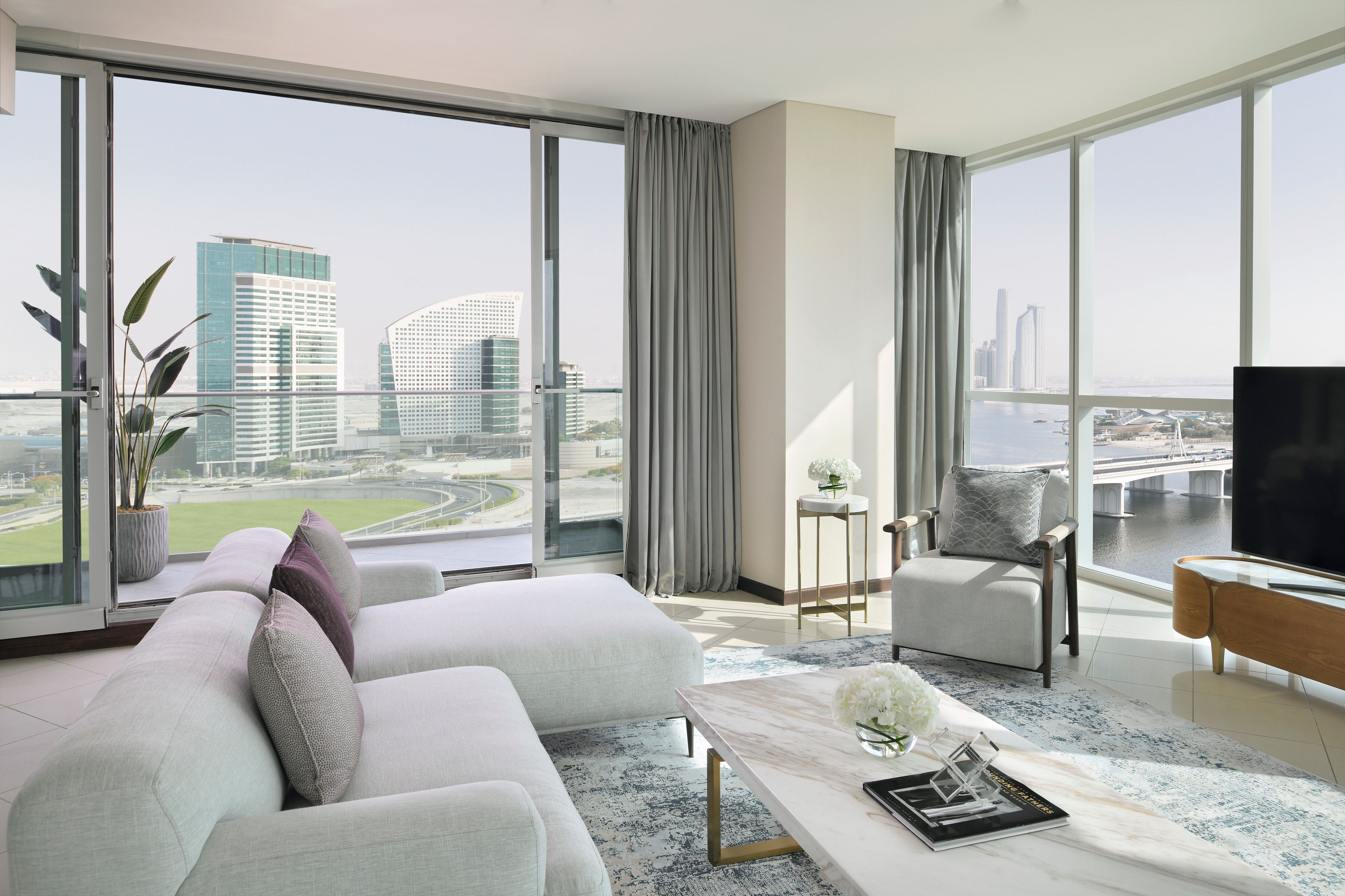 Un salon moderne avec vue sur la ville, comprenant un canapé, une table basse et un téléviseur.