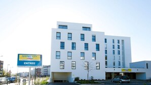 A modern multi-story building with a flat facade, multiple windows, and a parking area in front. - Appart'City Classic Rennes Beauregard (Rennes)