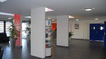 A modern lobby with a reception desk, a blue door, and a plant in the center.