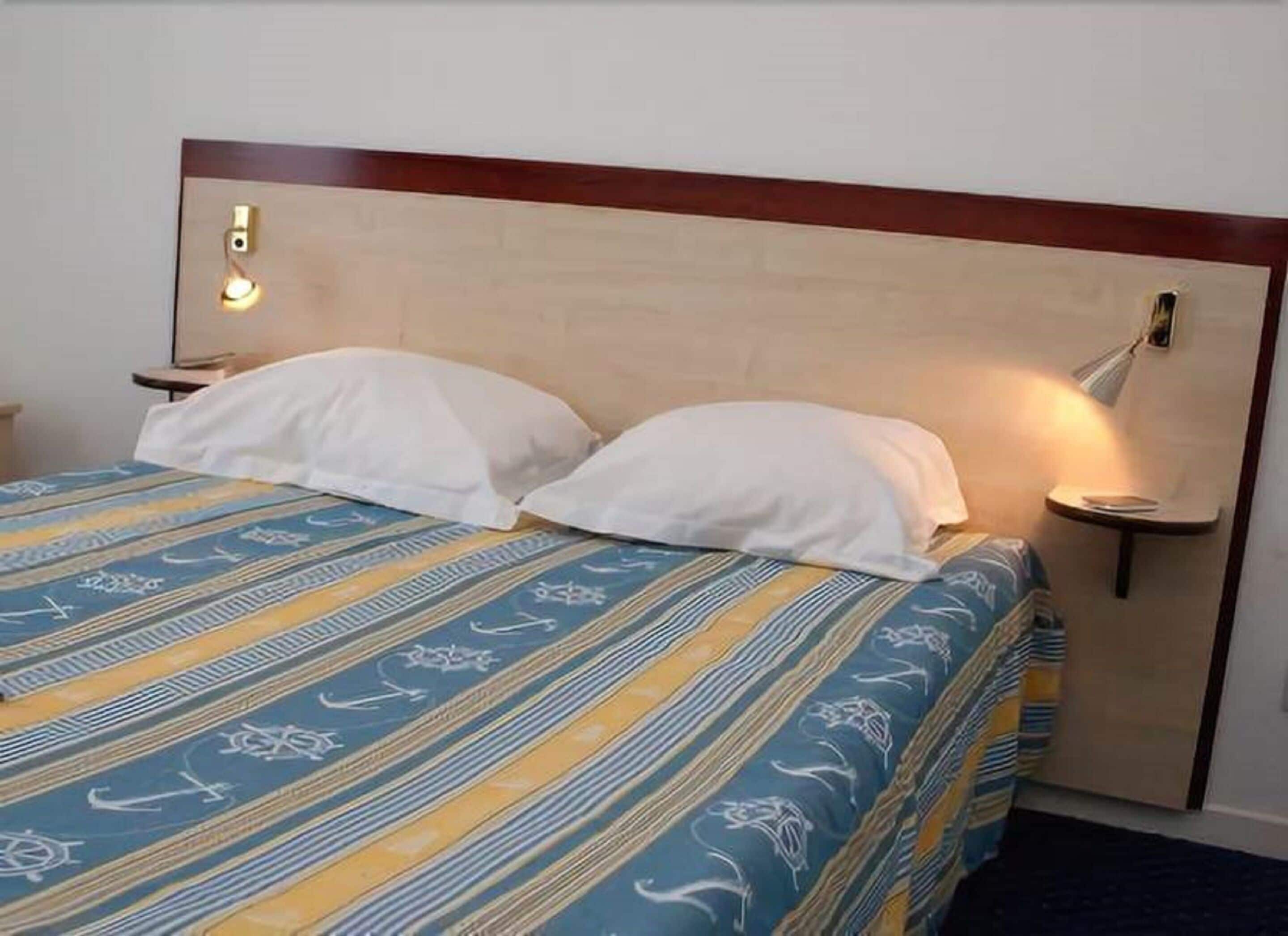A bed with a striped bedspread, two white pillows, a wooden headboard, and bedside lamps.