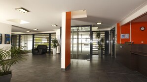 A modern lobby with a reception desk, seating area, and glass doors leading to another room. - Appart'City Classic Rennes Beauregard (Rennes)