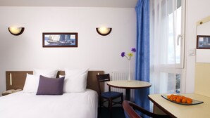 A hotel room with a bed, a chair, a small table, and a window with curtains. - Appart'City Classic Rennes Beauregard (Rennes)