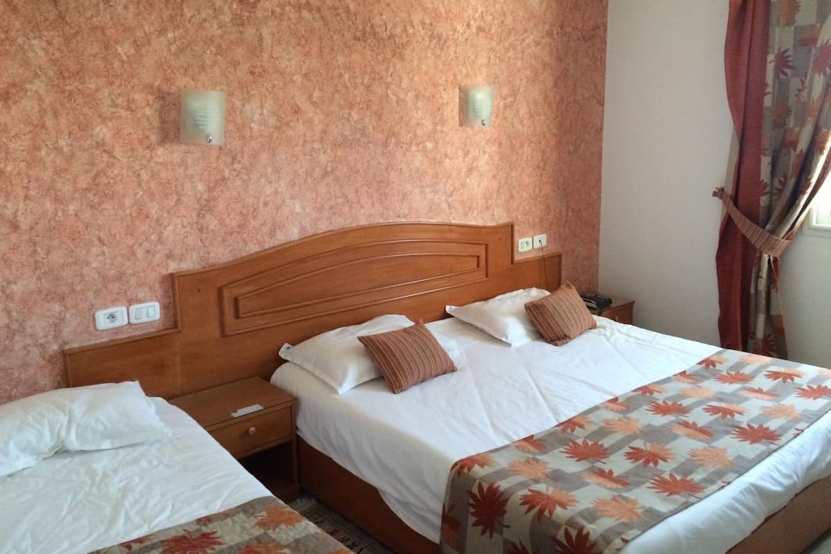 Ein Hotelzimmer mit einem hölzernen Kopfteil, zwei Betten, einem Nachttisch und einer gemusterten Bettdecke.