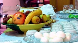 A room with a table set for a meal, featuring a bowl of fruit and various dishes.