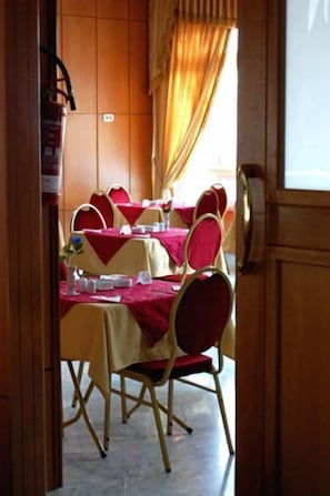 Un comedor con mesas dispuestas para comer, sillas y una ventana con cortinas.