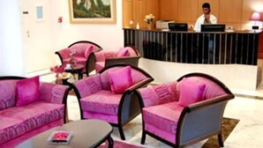 A hotel lobby with pink upholstered sofas, a reception desk, and a marble floor.