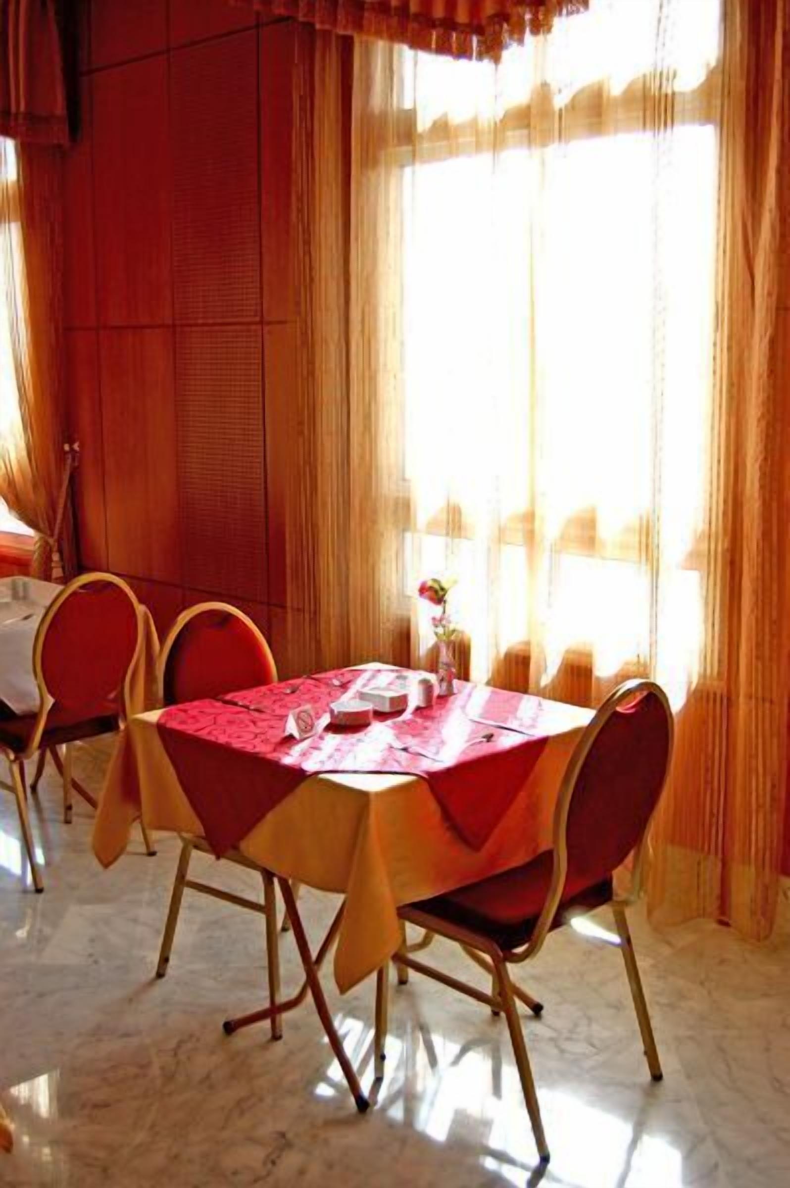 Comedor con mesa dispuesta para cuatro personas, sillas rojas y un florero con una flor.