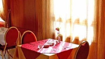 Comedor con mesa dispuesta para cuatro personas, sillas rojas y un florero con una flor.