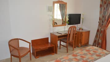 A bedroom with a bed, a desk, a chair, a television, and a mirror.
