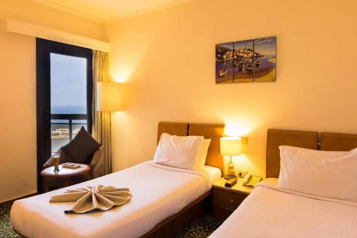 A hotel room with two beds, a nightstand with a lamp, a telephone, and a painting on the wall.