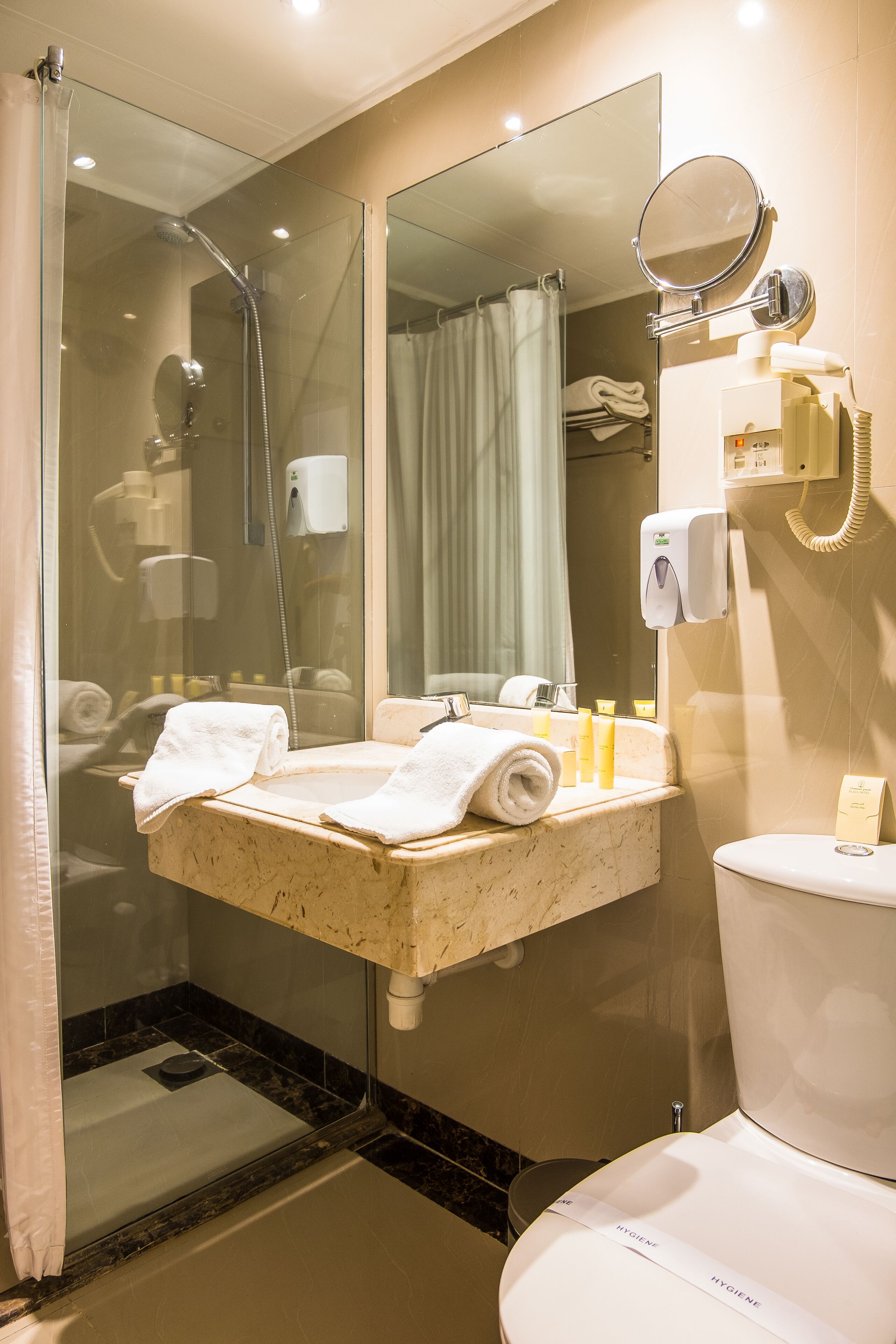A bathroom with a glass-enclosed shower, a sink with toiletries, a toilet, and a mirror.