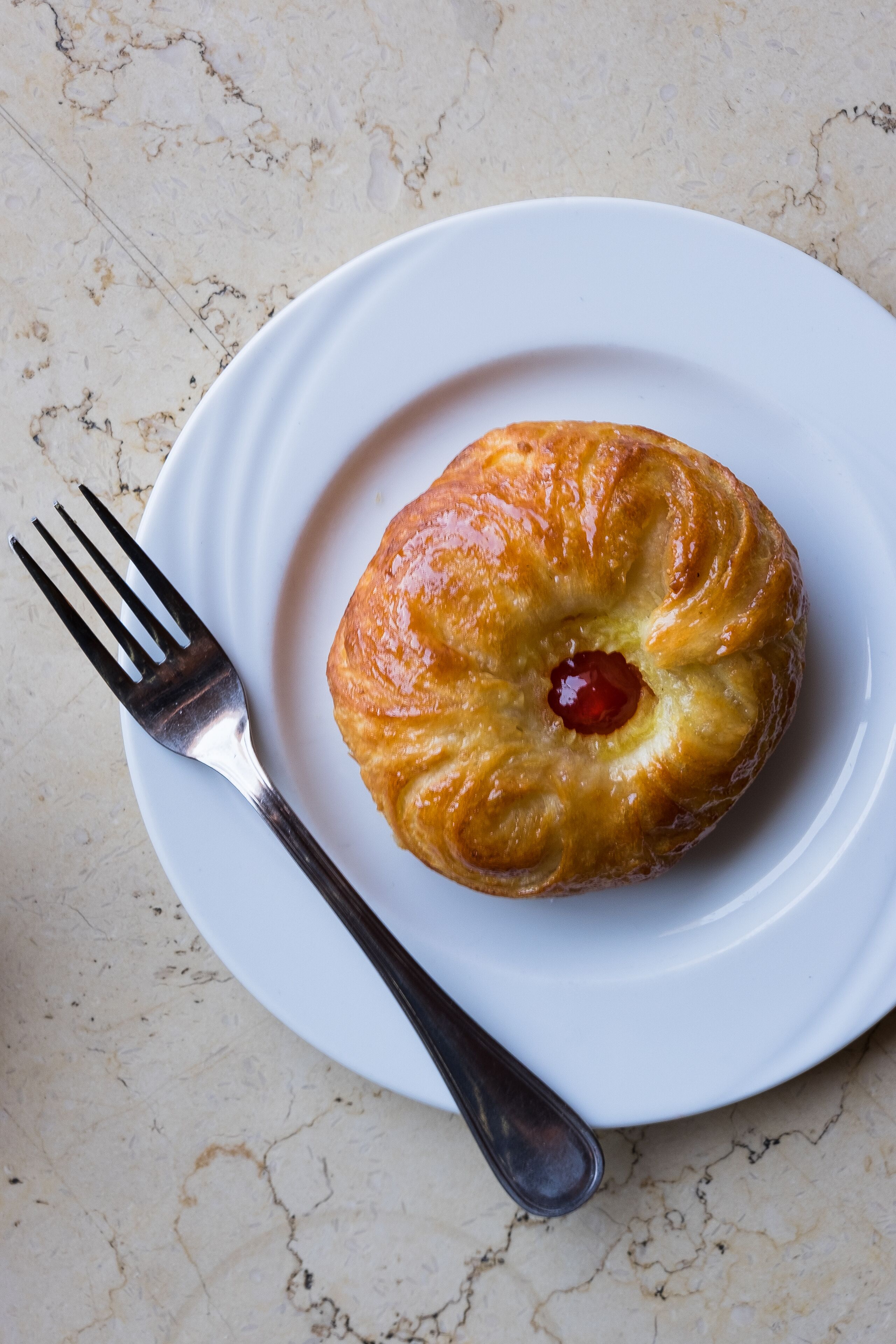 A round pastry with a red filling on a white plate, accompanied by a fork.