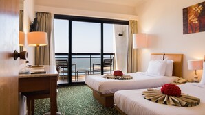 Une chambre d’hôtel avec deux lits, un bureau et une vue sur la mer.
