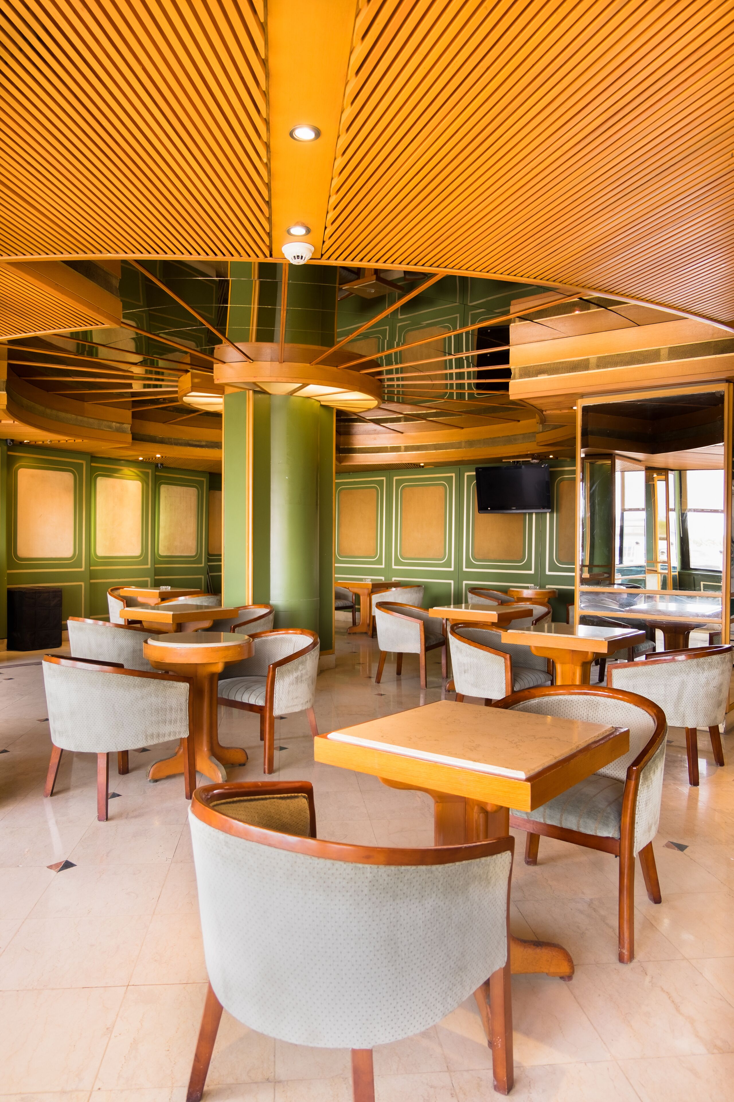 A restaurant with multiple tables and chairs, a green and yellow color scheme, and a modern ceiling design.