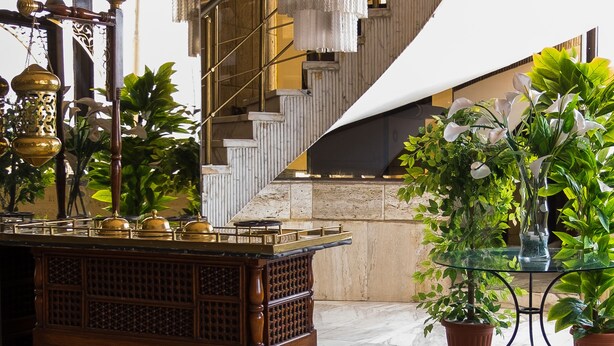 Un hall d’entrée avec un sol en marbre, un chariot en bois, des plantes en pot, un escalier et un lustre.