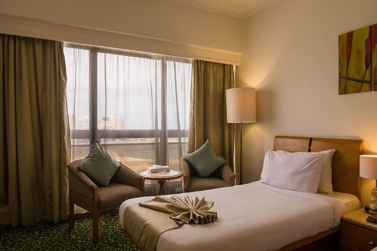 A hotel room with a bed, a chair, a small table, and a lamp.