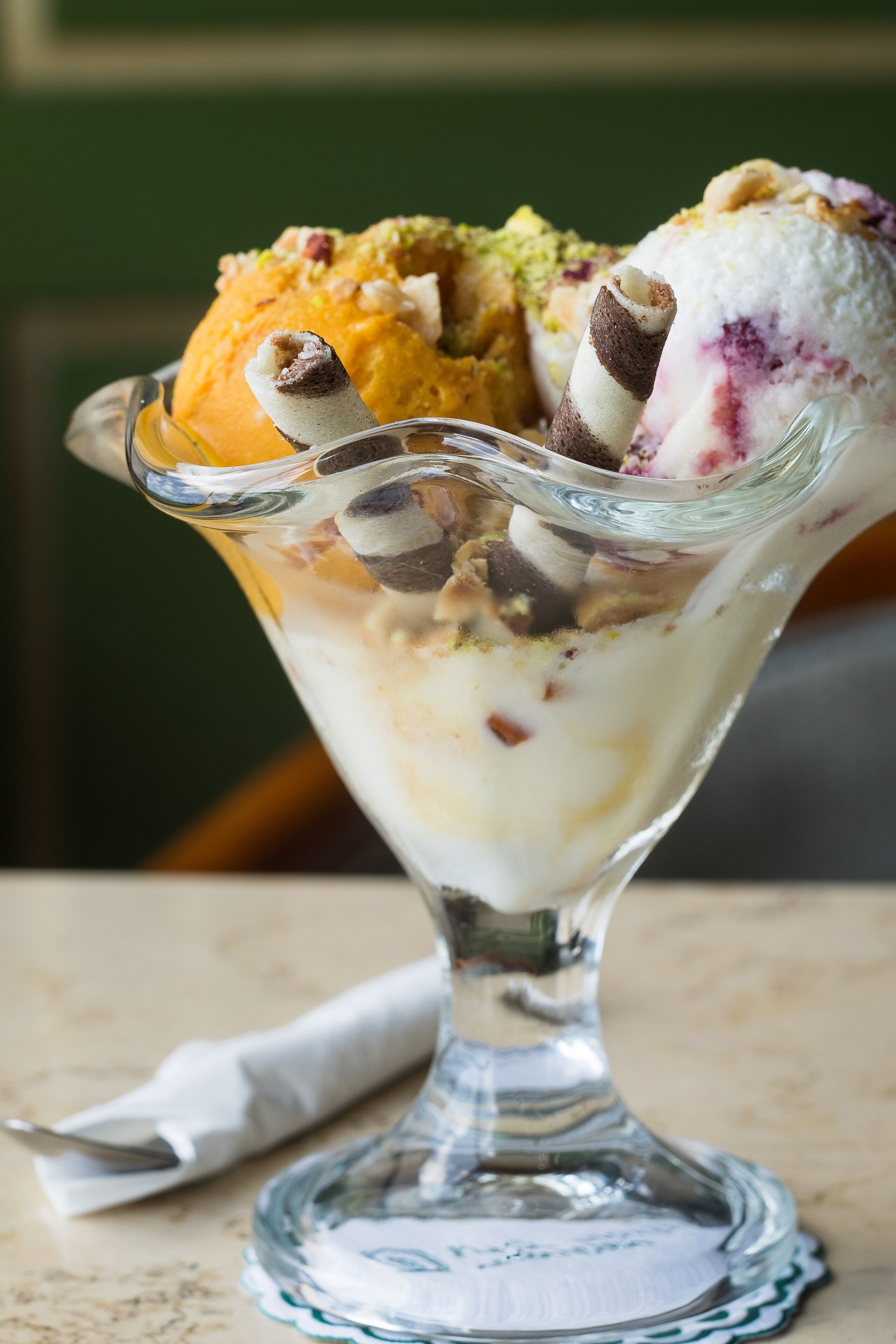 A dessert in a glass bowl with multiple scoops of ice cream and toppings.