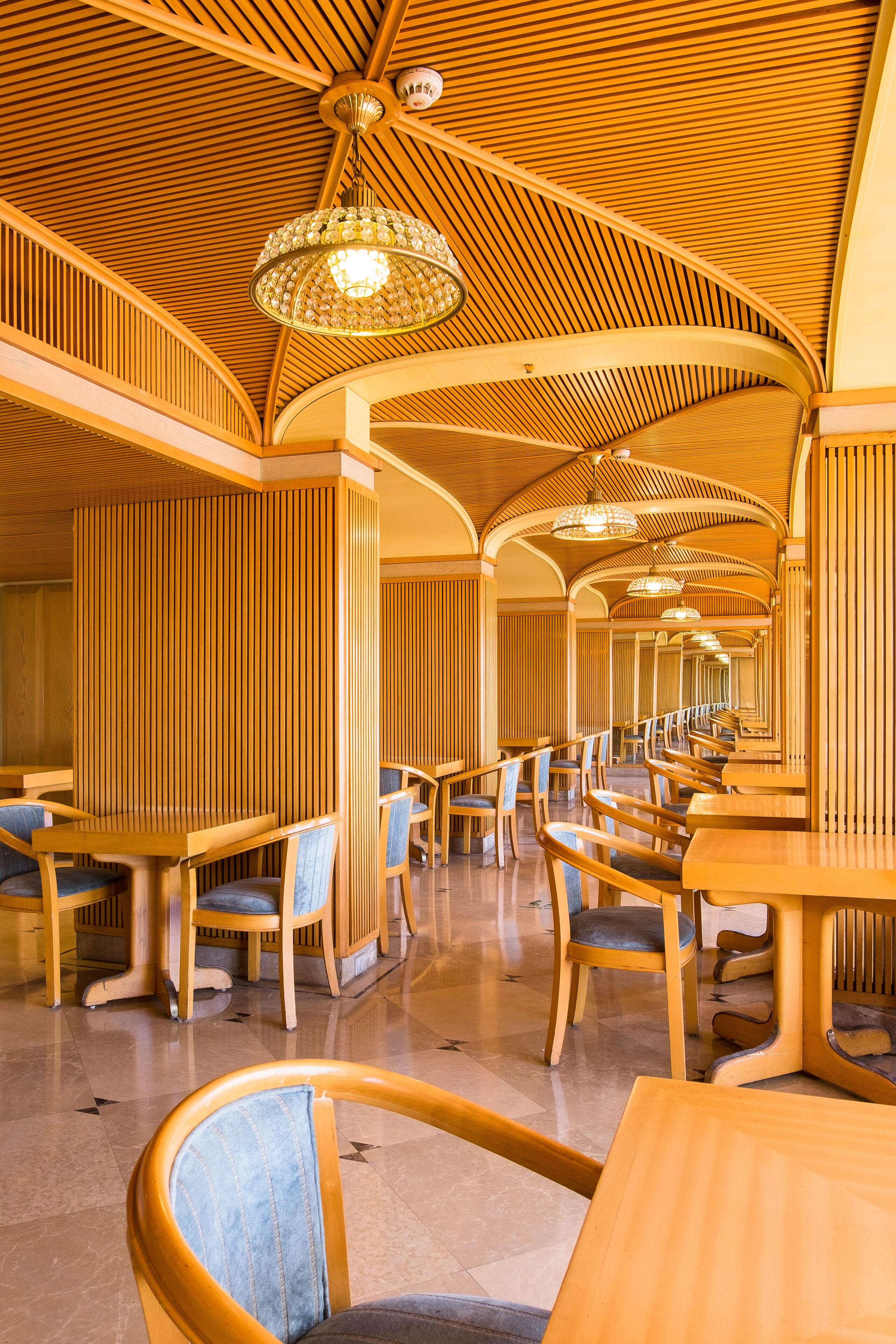 Un restaurante espacioso con paneles de madera, techo curvo y varias mesas y sillas para comer.
