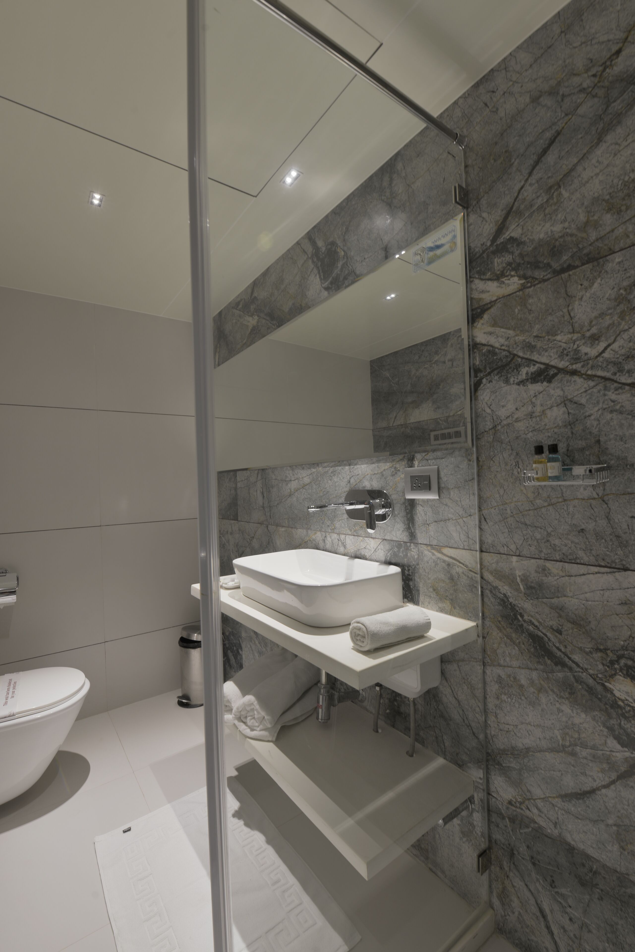 A modern bathroom with a glass-enclosed shower, a white sink, and a marble backsplash.