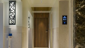 A modern hotel corridor with a marble floor, a wooden door at the end, and a digital sign indicating room G-1. - Hotel Airlink (Mumbai)