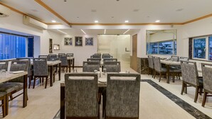 A spacious dining area with multiple tables and chairs, a marble floor, and a large mirror on the wall. - Hotel Airlink (Mumbai)