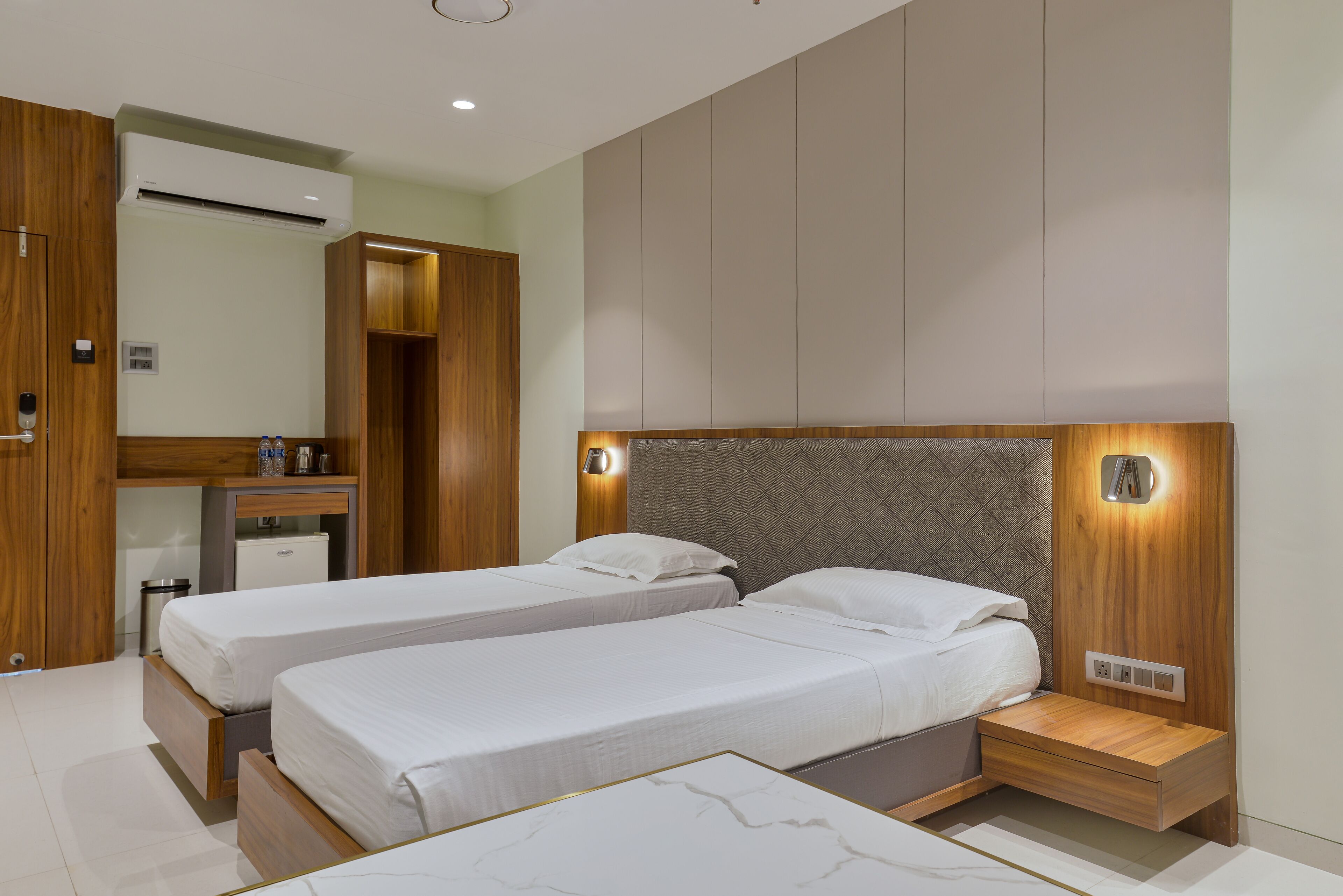 Habitación de hotel con dos camas, un armario de madera, un escritorio y un equipo de aire acondicionado instalado.