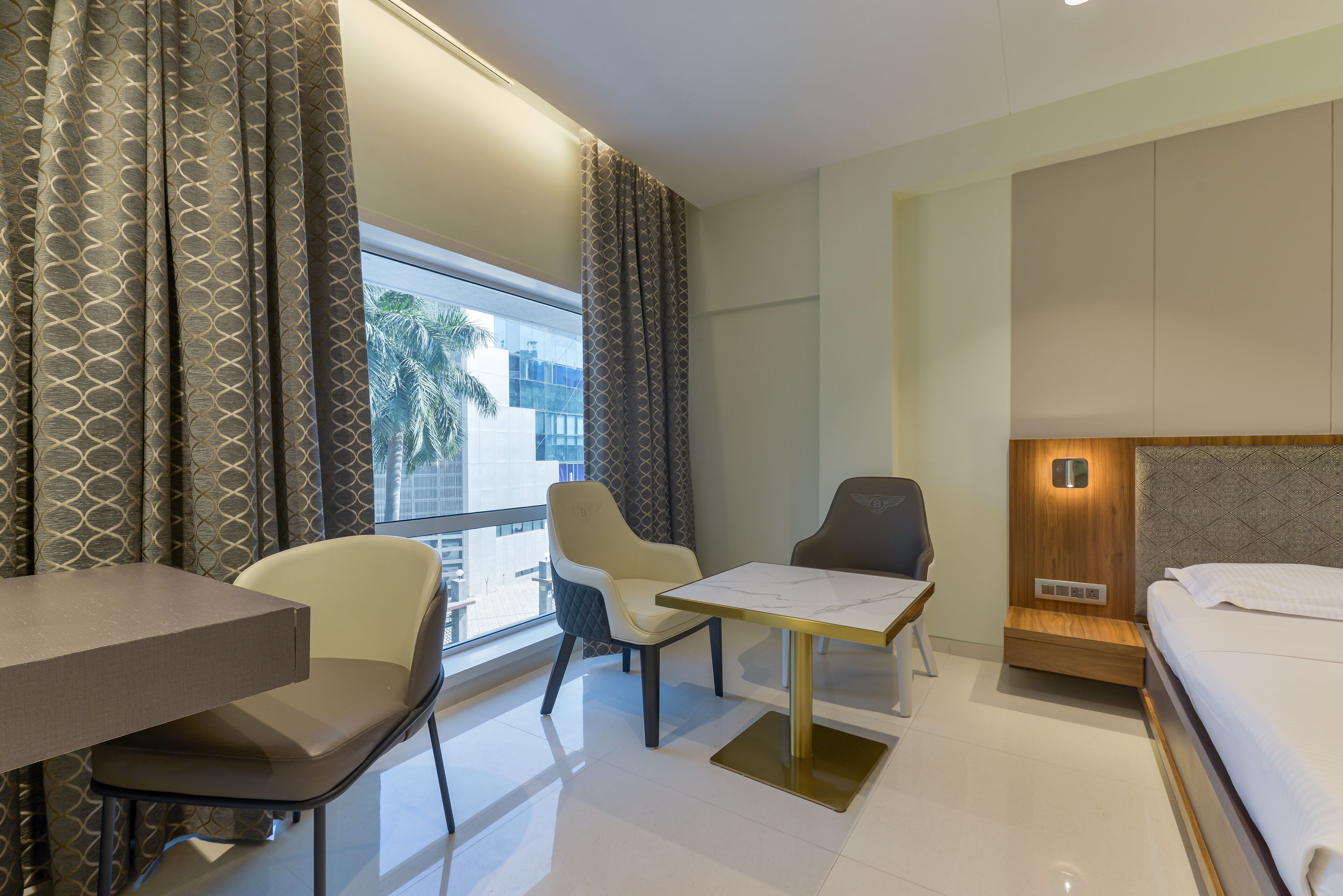 A hotel room with a bed, a desk, two chairs, a small table, and a window with curtains.