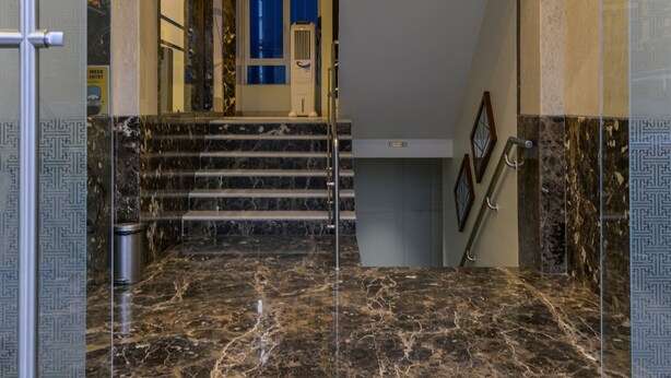 A modern interior with marble flooring, glass doors, and a staircase leading to a room with a blue door. - Hotel Airlink (Mumbai)