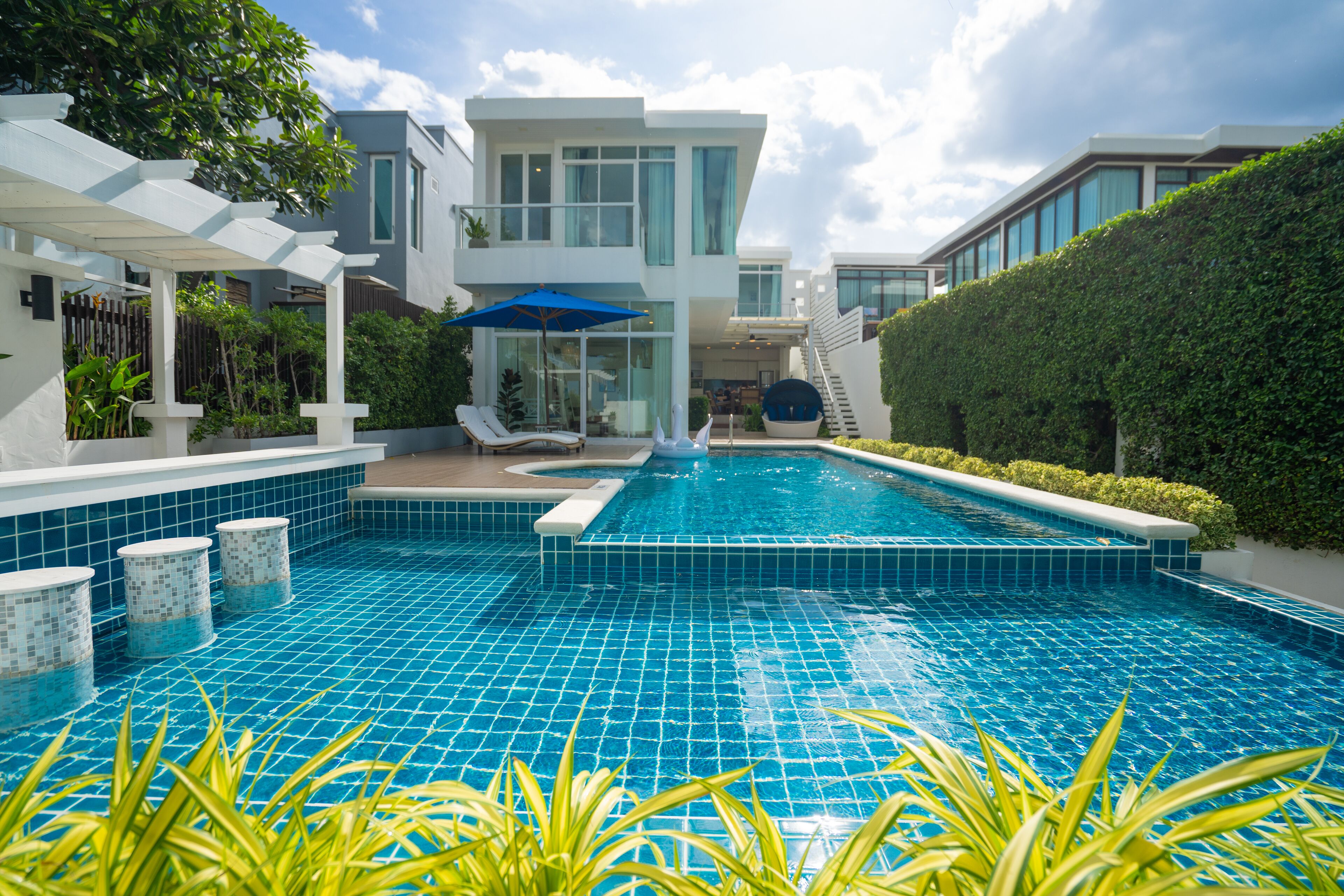 A modern pool area with a clear blue pool, lounge chairs, and a covered seating area.