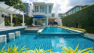 A modern pool area with a clear blue pool, lounge chairs, and a covered seating area.