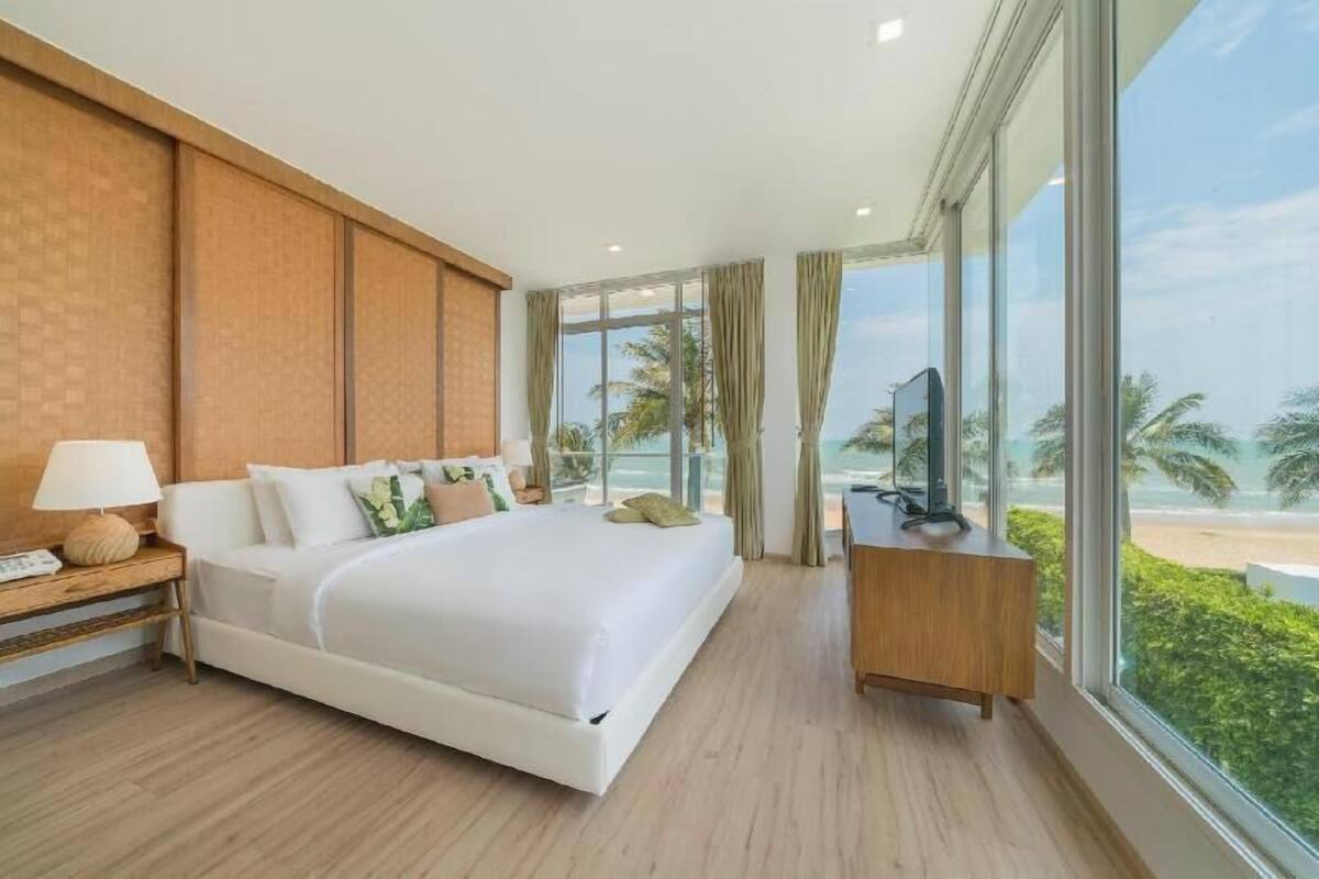 A modern hotel room with a large bed, a TV on a wooden side table, and a view of the beach.