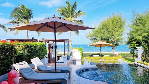 A poolside area with lounge chairs, umbrellas, and a view of the sea. - Tolani Le Bayburi Villas Pranburi (Pranburi)