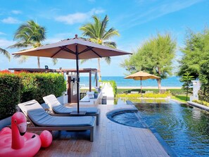 Un espace aménagé au bord de la piscine, avec des chaises longues, des parasols et une vue sur la mer.