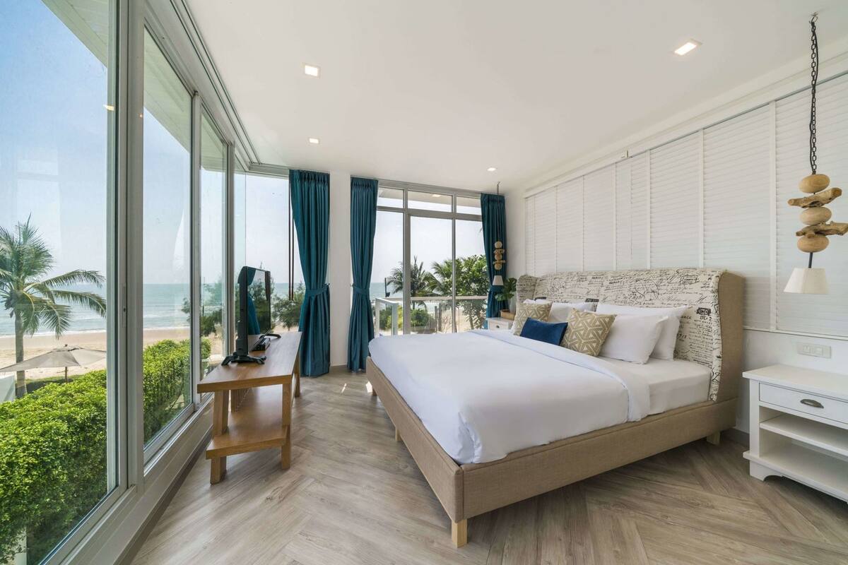 A modern hotel room with a large bed, a desk, and a view of the beach.