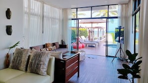 A spacious living area with a sofa, coffee table, and a view of a pool and outdoor seating. - Tolani Le Bayburi Villas Pranburi (Pranburi)